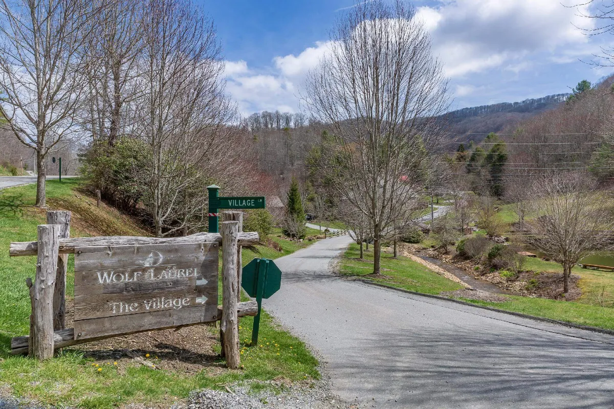 An inviting exterior shot of the 'Wolf Laurel' sign and directional sign to the village, nestled among trees and rolling hills. The natural setting and signage highlight the sense of arrival and exploration in the local area.