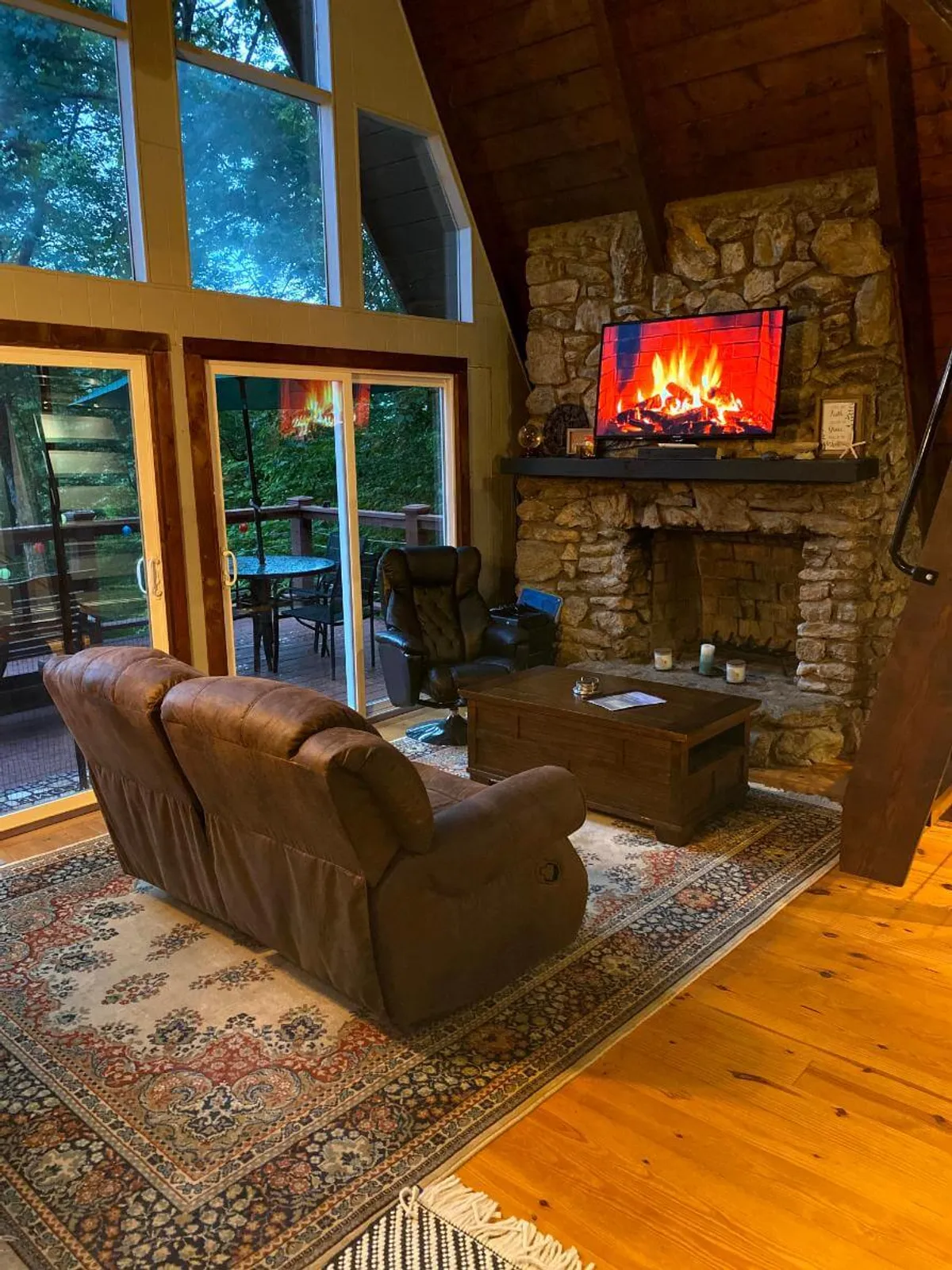 A spacious, inviting interior with a stone fireplace, large windows offering scenic views, comfortable seating, and a TV with a fire display. The mood is warm and communal, ideal for family gatherings, relaxation after a day outside, and creating lasting memories.