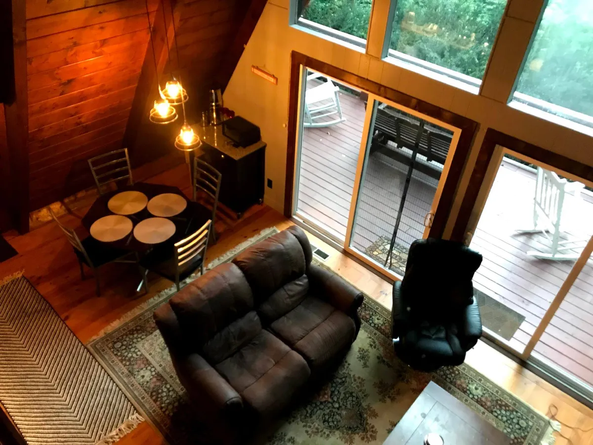 A wide shot showcasing the open living and dining area, with a spacious sofa, a large dining table, and expansive windows letting in natural light. The arrangement encourages interaction, whether guests are lounging, dining, or planning the next adventure together.