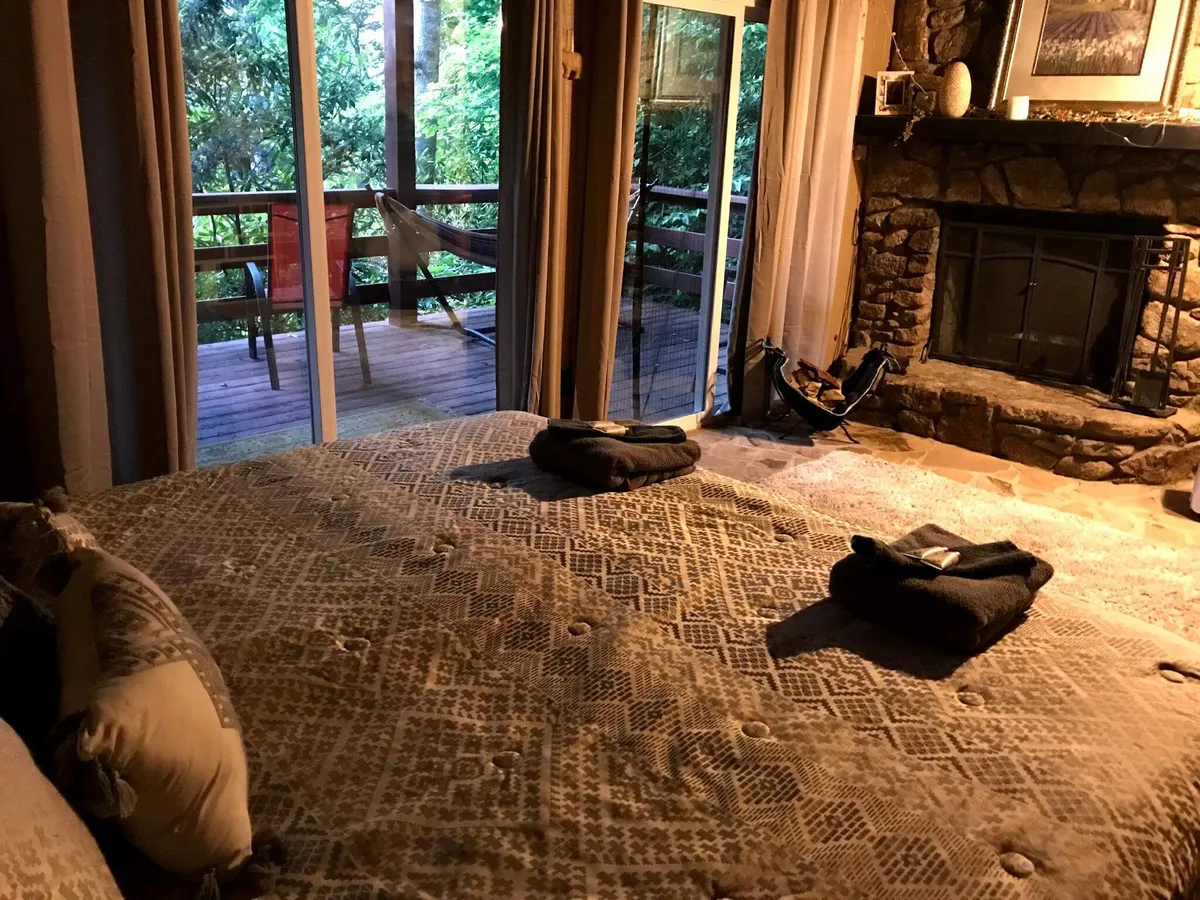 A tranquil bedroom with a stone fireplace and large glass sliding doors leading directly to the deck, providing a glimpse of the outdoor scenery. This setup showcases the ease of transitioning from indoor comfort to the outdoor deck.
