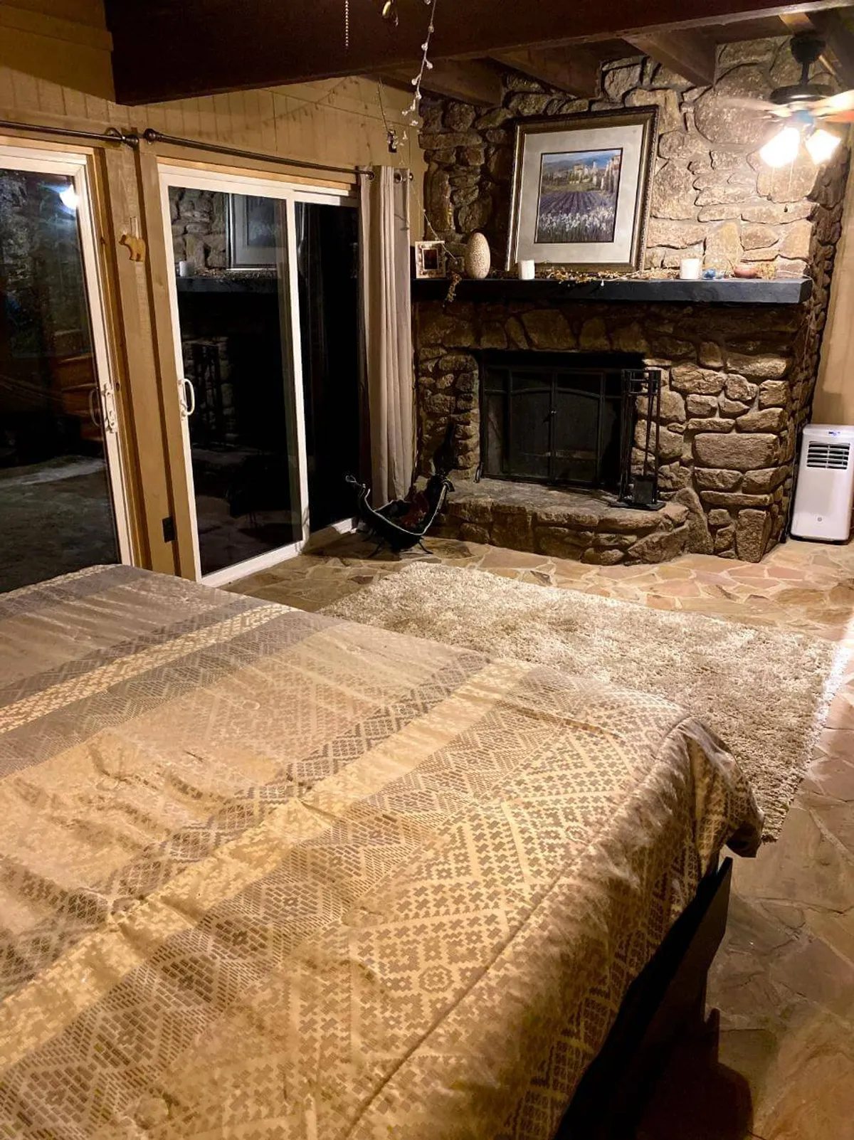 A cozy room featuring a stone fireplace, a bed with a charming patterned cover, and a large window with curtains. The room feels intimate and warm, with natural light filtering in and the fire casting a gentle glow—perfect for snuggling up after a day outdoors.