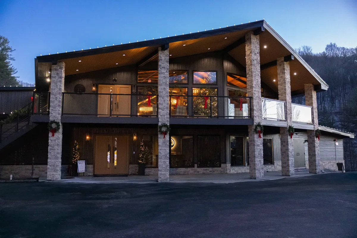 This exterior image shows the inviting entrance to the resort, with large glass windows, stone columns, festive outdoor lighting, and a decorated entryway. The scene suggests warmth and excitement, hinting at gatherings and special events inside.